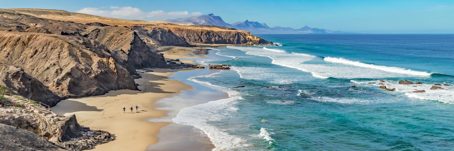 A beach in Spain with blue sea to the right and rocky cliffs to the left