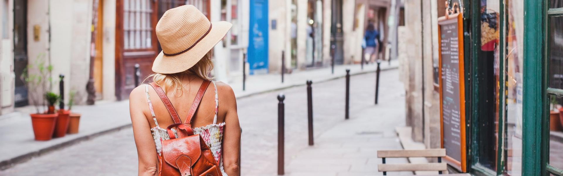 A woman with a hat and backpack walks away down a colourful street