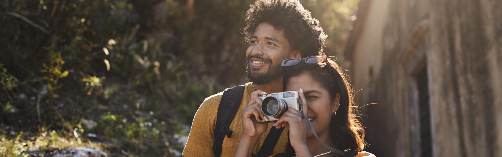 Young woman photographing through camera by boyfriend on sunny day during vacation