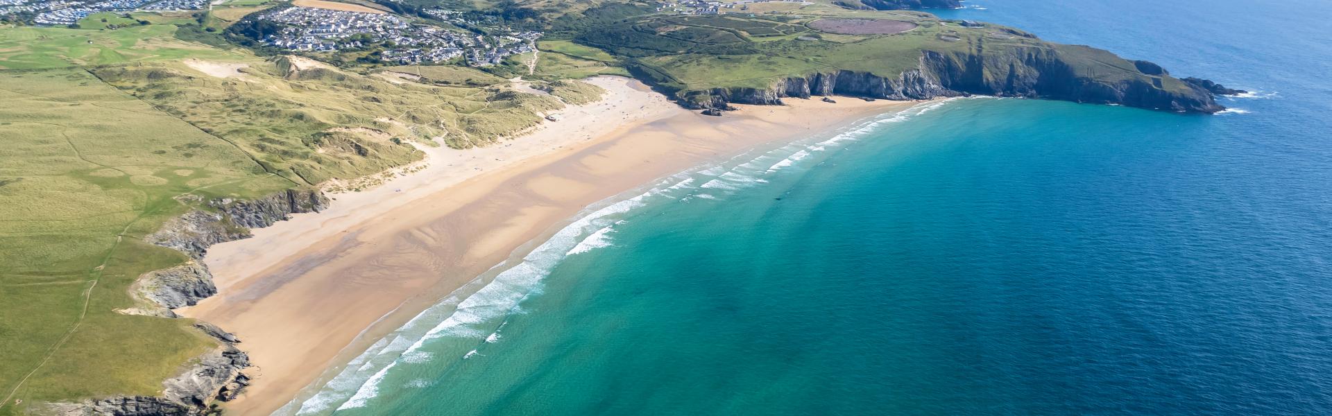 A bird's eye view of a golden sands beach surrounded by fields and the ocean