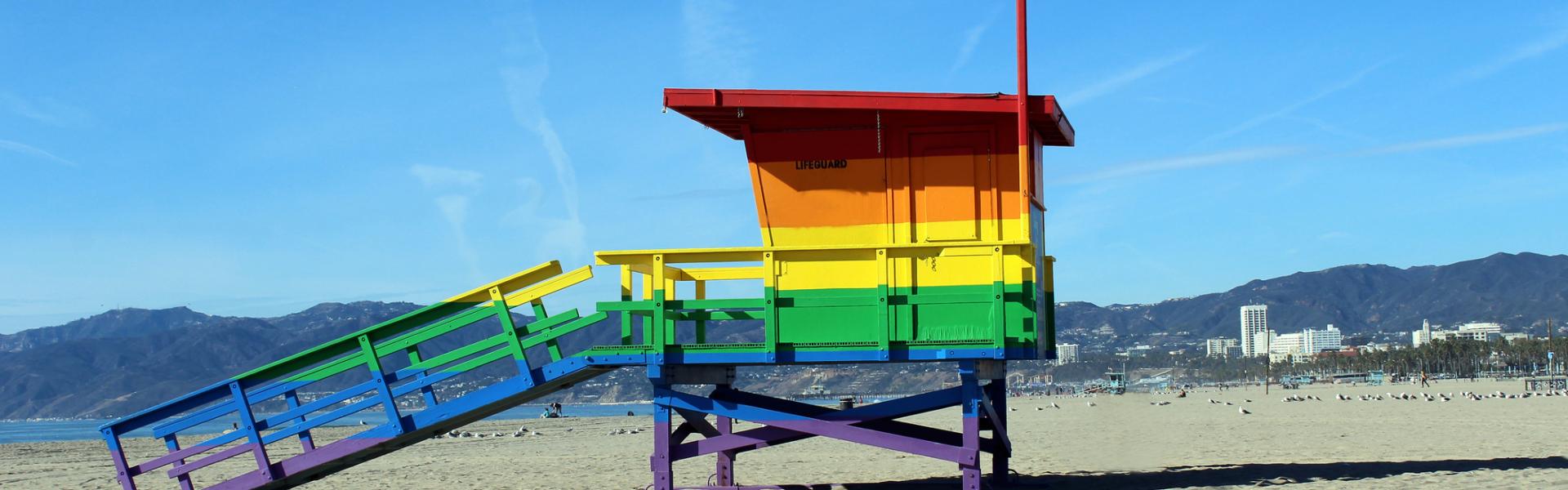 View of a wooden hut painted in rainbow colors standing on a beach.