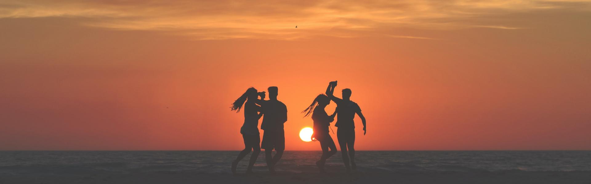 silhouette photo of four people dancing on sands near shoreline