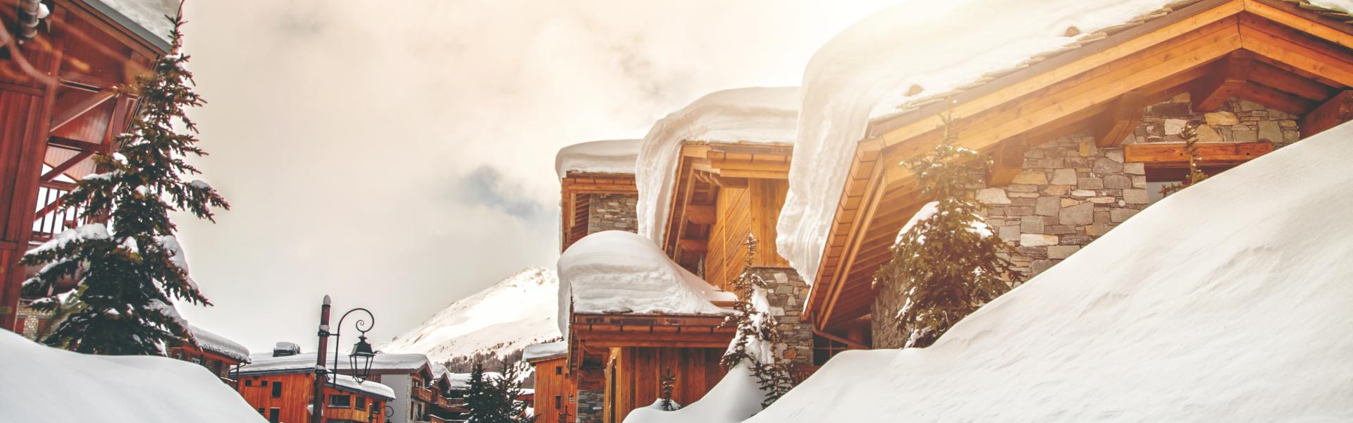 Taken from street. Color photography of several common wooden chalet and fresh snow footpath in french ski resort of Val d'Isere during a beautiful sunny day in january. This image was taken in winter season in Val d'Isere, a french famous ski resort village in Tarentaise mountains, in Savoie, Auvergne-Rhone-Alpes region in European Alps.