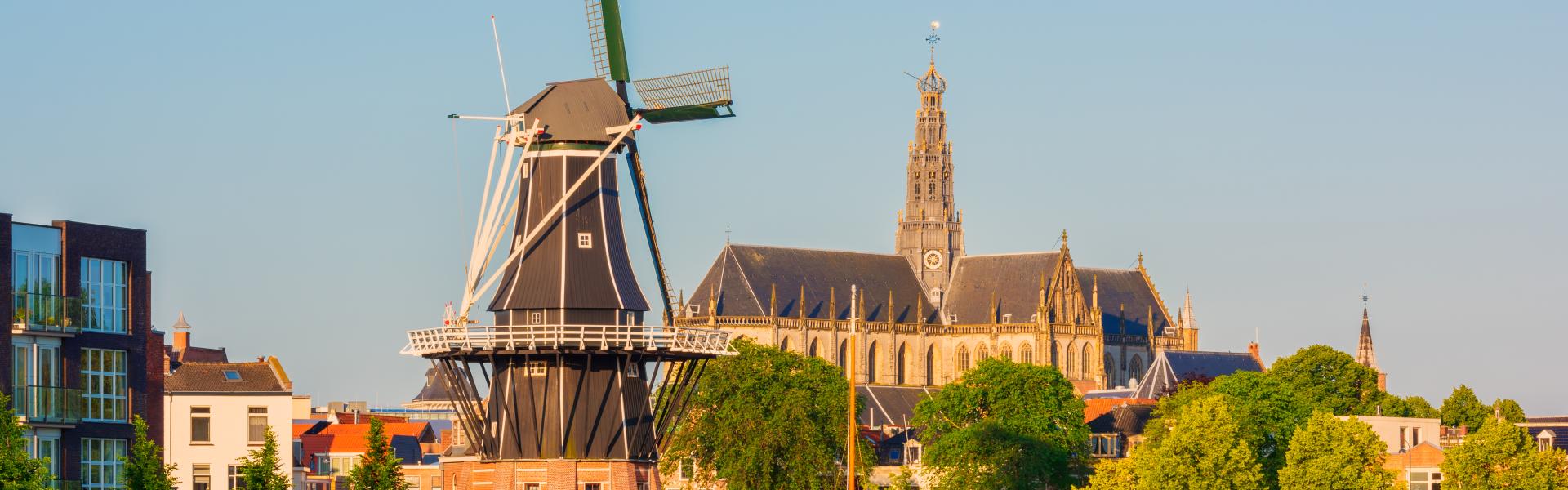 Skyline of Haarlem, North Holland, Netherlands around sunrise, with Windmill "De Adriaan" from 1779 and 13th Century Saint Bavo Church. The Spaarne river flows through Haarlem.