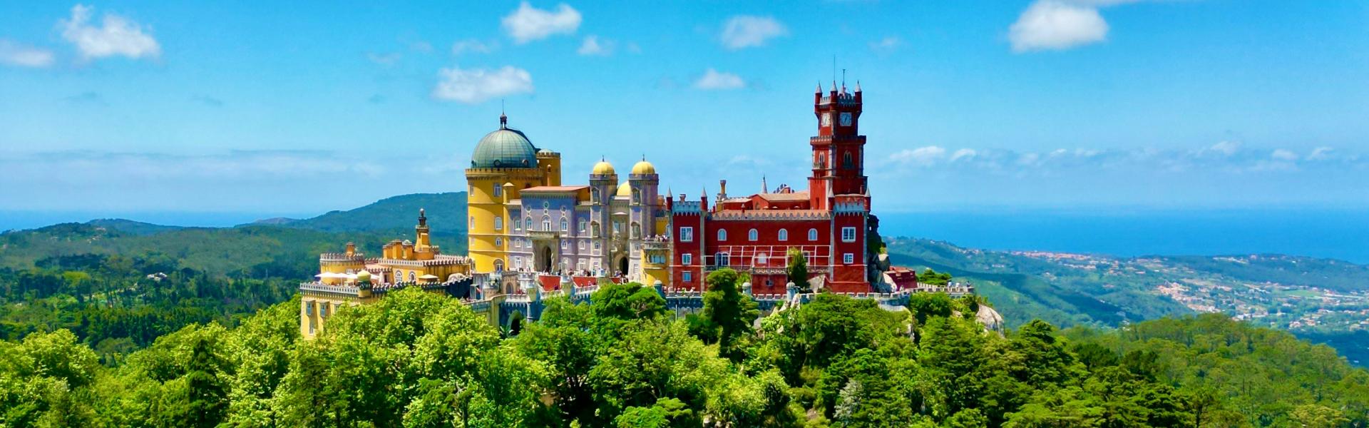 A colorful castle on a hilltop surrounded by green trees