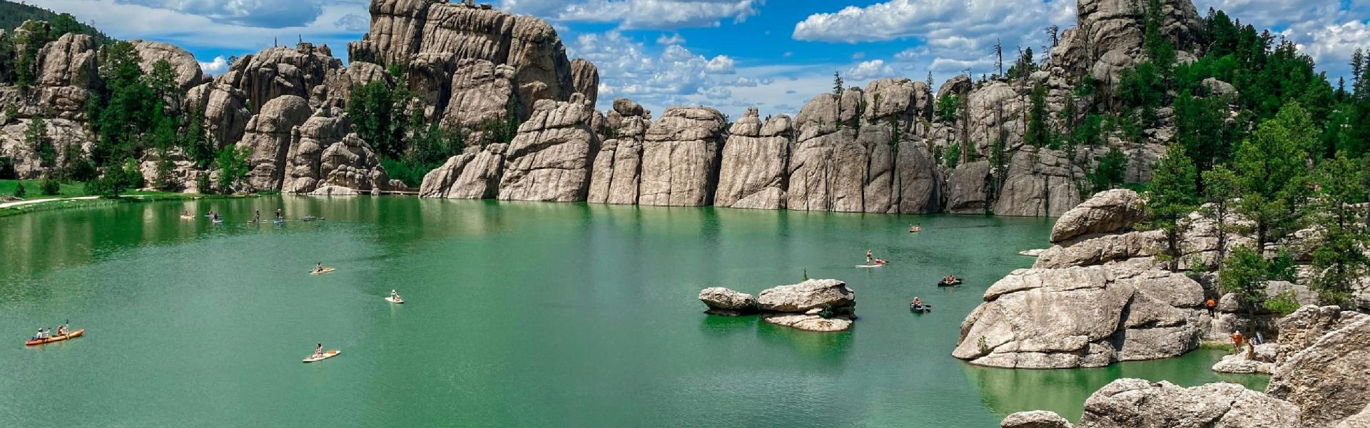 A green-blue lake in front of a grey rock formation under a bright but cloudy sky