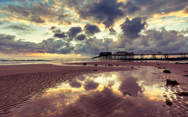 A dramatic cloudy sky over a beach with a pier at sunset