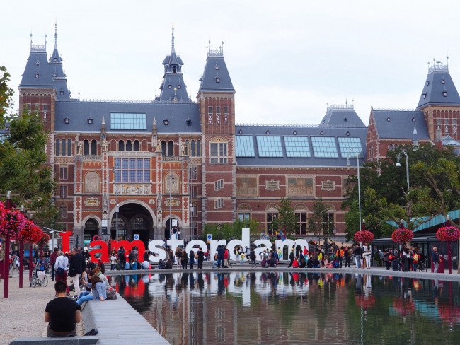 People surrounding a sign that says I Am Amsterdam, with the Rijksmuseum in the background