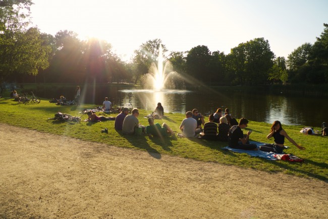 Menschen sitzen bei Sonnenuntergang im Gras an einem See