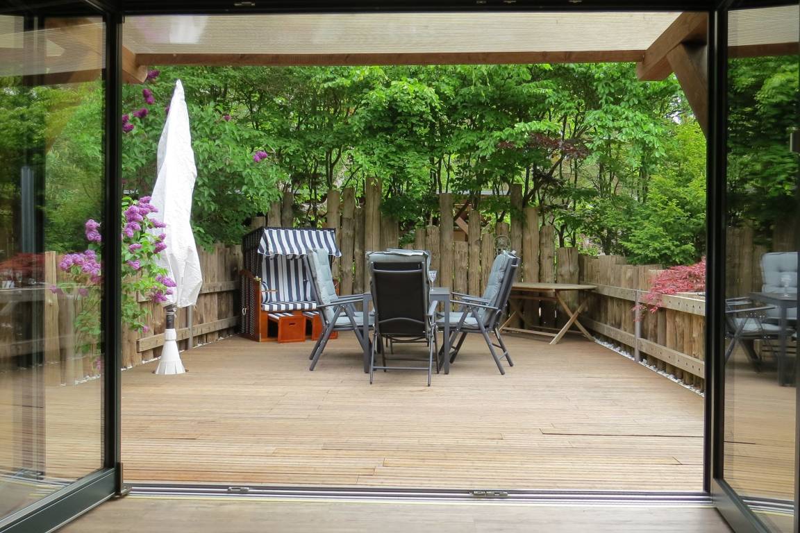 Terrasse mit Tisch und Stühlen, umgeben von grünen Pflanzen. [Strandhaus Möve] [Wustrow]