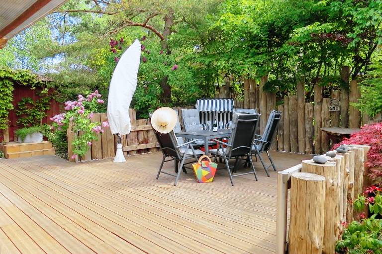 Holztisch mit Stühlen auf Terrasse, umgeben von Bäumen. [Strandhaus Möve] in [Wustrow].